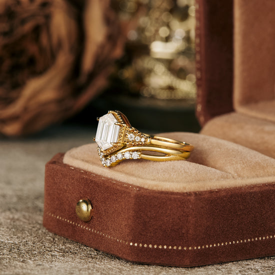 Elegant long-hexagon Moissanite ring set in gold resting in velvet jewelry box.