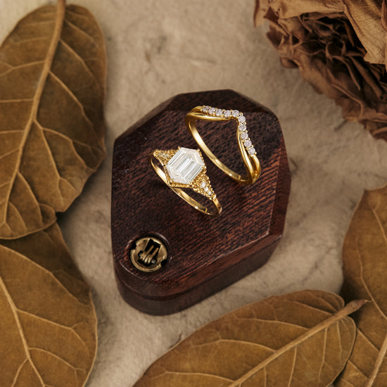 Gold long-hexagon Moissanite ring set displayed on wooden box with dried leaves.