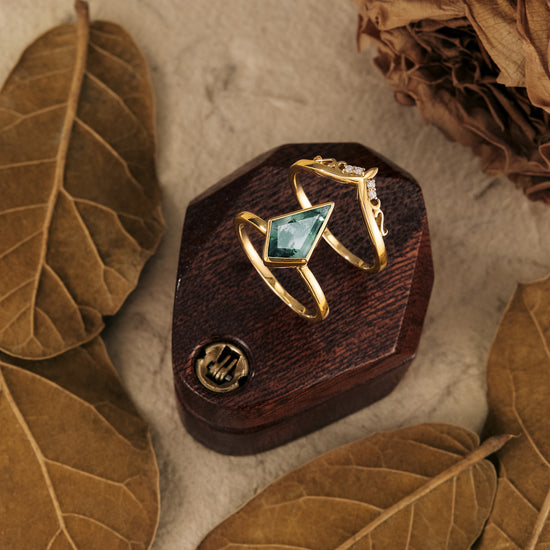 Kite-cut moss agate ring set in gold with intricate leaf accents on a wood display.