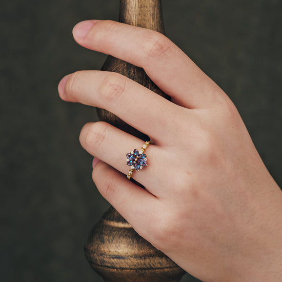 Chrysanthemum-inspired six-stone engagement ring with lab alexandrite on hand.