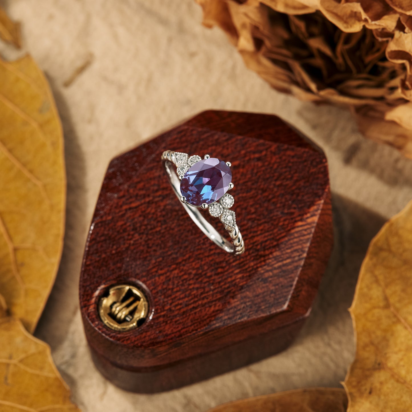 Twisted engagement ring with oval alexandrite and moissanite accents on wooden box.