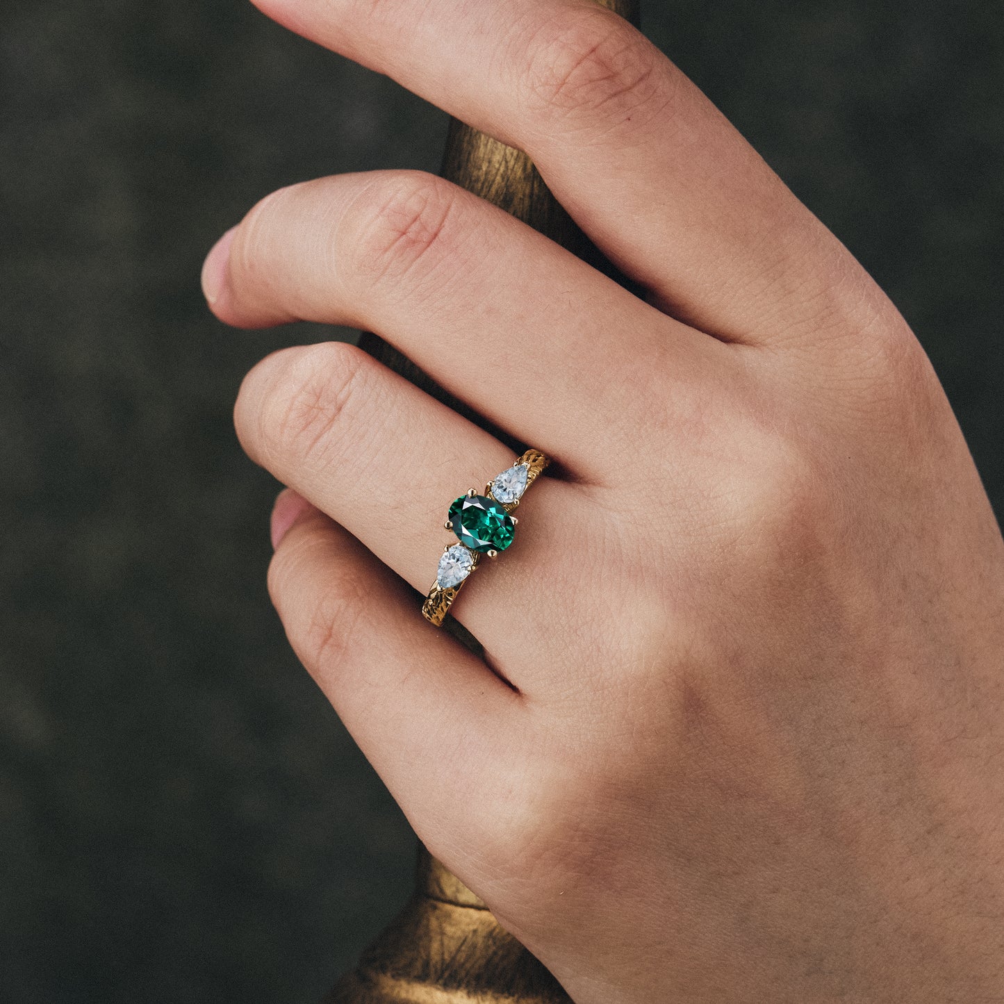 Hand wearing emerald and aquamarine cluster ring on a gold band.