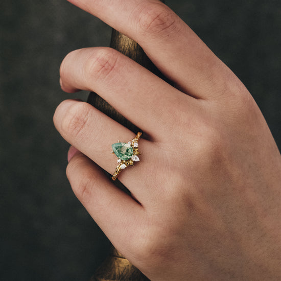 Moss agate pear ring with diamond accents on a hand, featuring a leaf-inspired band.