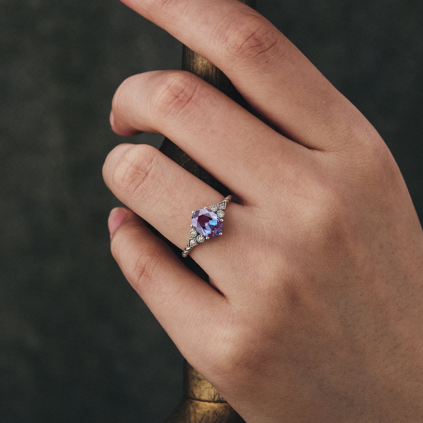 Hand wearing unique oval alexandrite twisted engagement ring with moissanite stones.